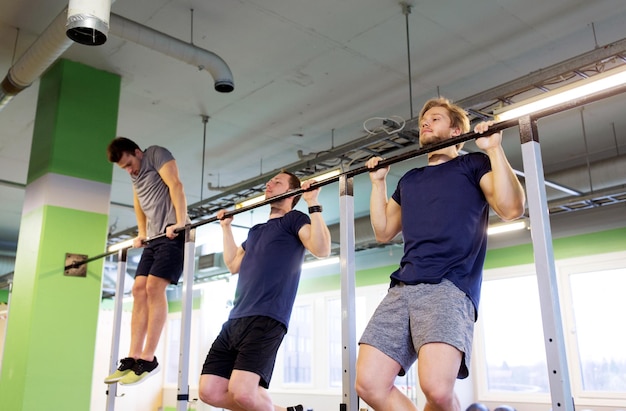 sport, fitness and people concept - group of young men exercising and doing pull-ups on horizontal bar in gym