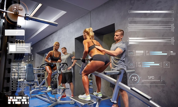 sport, fitness, sporten en mensenconcept - jonge vrouw en personal trainer die spieren buigen op de sportschoolmachine via virtuele grafieken