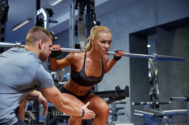 sport, fitness, teamwork, bodybuilding and people concept - young woman and personal trainer with bar flexing muscles in gym