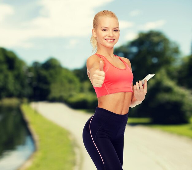 sport, fitness, technology, internet and healthcare concept - smiling sporty woman with smartphone showing thumbs up