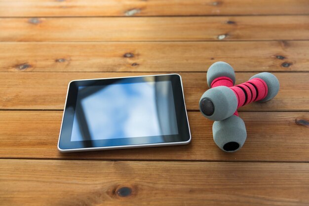 sport, fitness, technology and objects concept - close up of dumbbells and tablet pc computer on wooden floor