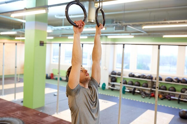 Фото Концепция спорта, фитнеса, тренировок и людей - мужчина тренируется и подтягивается на кольцах в тренажерном зале