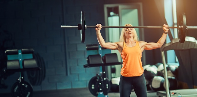 Sport, fitness, training en geluk concept - sportieve vrouw met barbell in sportschool