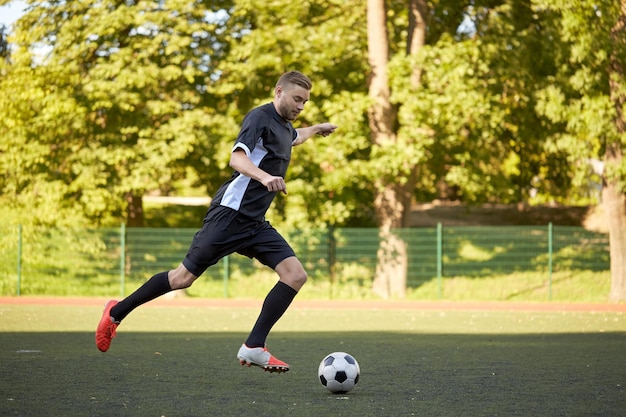 sport, football training and people - soccer player playing with ball on field