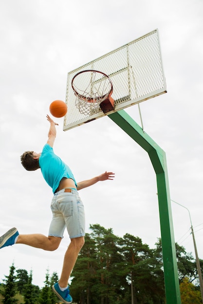 sport, game and basketball concept - young man throwing ball into basket outdoors