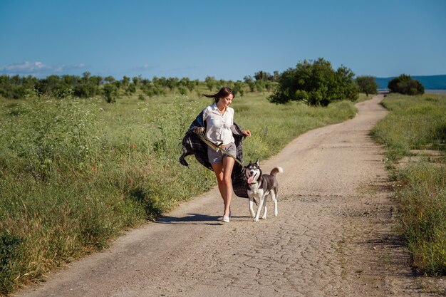 スポーツの女の子は、犬と一緒に道路でシベリアンハスキーを実行しています