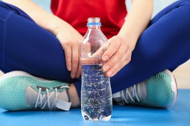 Sport girl sitting and holds bottle with water, close up