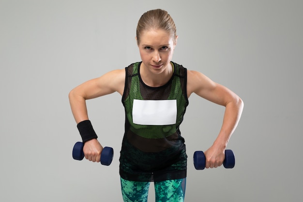 Sport girl in sportswear holds a dumbbell on a gray