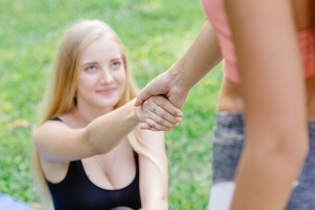 スポーツの女の子の十代の若者は、友人がサポートとトレーニングのためにお互いを引っ張って手を握るのを手伝います。