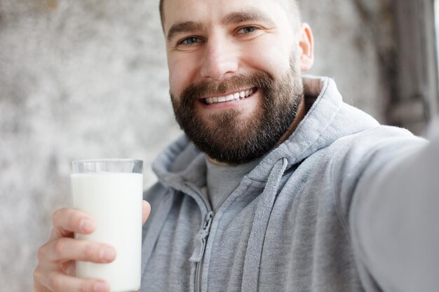 Sport, health, people, emotions, 4K and lifestyle concept - Young man drinks and lick off white mustache. young man drinks smoothie bit of whipped cream stays on his face after he finishes drinking