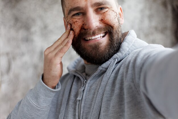 Photo sport, health, people, emotions, lifestyle concept - handsome man with three different face masks chocolate, cream and clay masks. photo of man with perfect skin. grooming himself