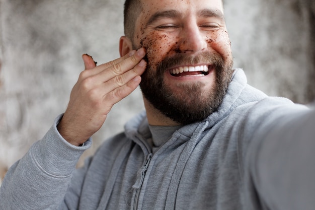 Sport, health, people, emotions, lifestyle concept - Handsome man with three different face masks chocolate, cream and clay masks. Photo of man with perfect skin. Grooming himself