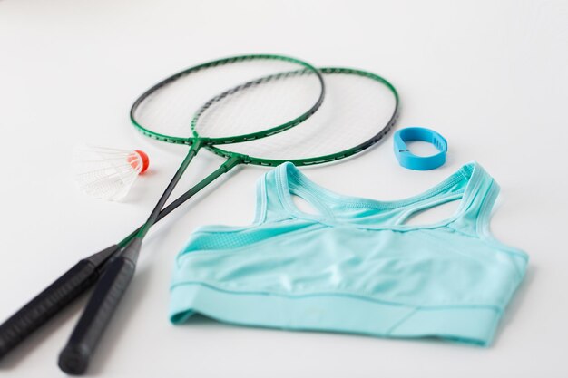 sport, healthy lifestyle and objects concept - close up of badminton rackets with shuttlecock, fitness tracker and sports top