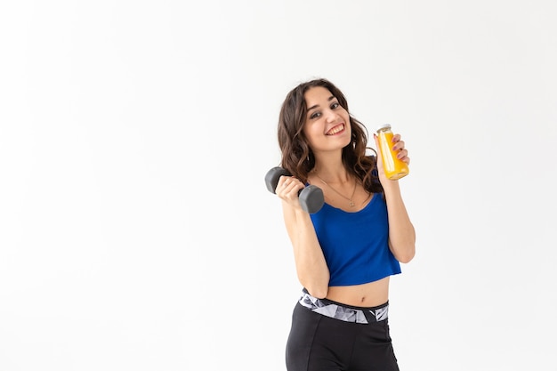 Sport, healthy lifestyle, people concept - young woman holds bottle of juice and a dumbbell on white background with copy space.