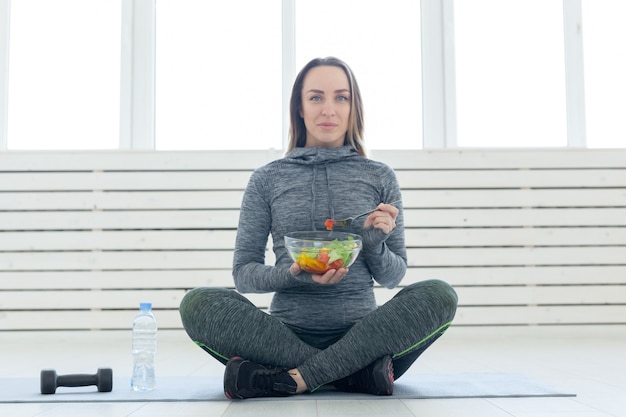 Sport healthy lifestyle and people concept young woman with salad and a dumbbell sitting on the