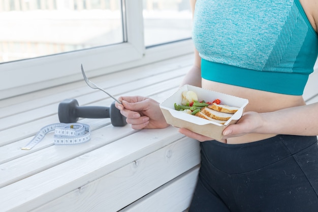 Photo sport, healthy, people concept - close-up of girl holding salad and dumbbell after fitness training