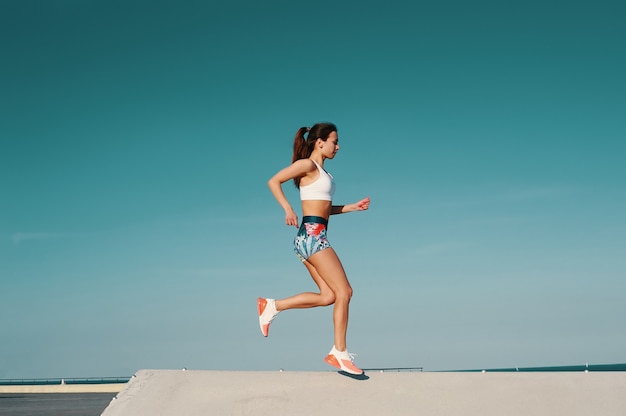 スポーツは彼女の生き方です。屋外で運動しながらジョギングスポーツ服の美しい若い女性の全長