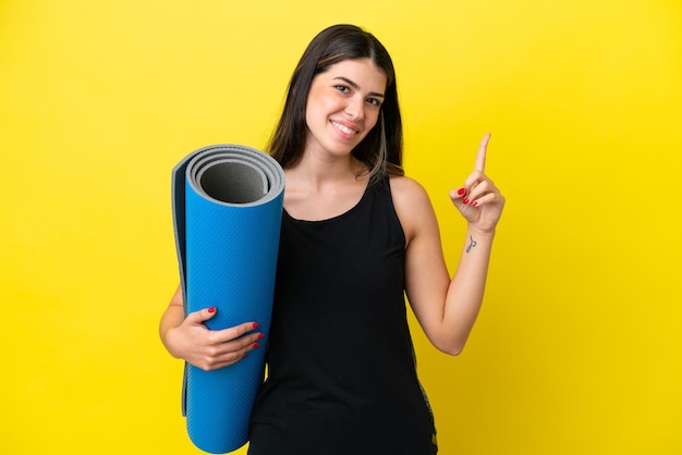 Sport Italiaanse vrouw die naar yogalessen gaat geïsoleerd op een gele achtergrond die een vinger toont en opheft in teken van het beste