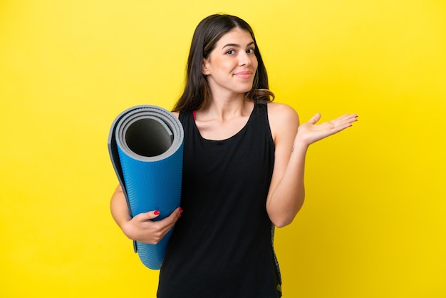 Sport Italian woman going to yoga classes isolated on yellow background having doubts while raising hands