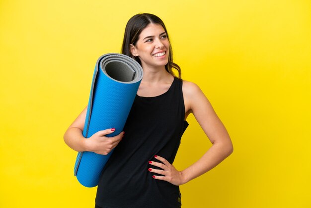 Sport Italian woman going to yoga classes isolated on yellow background posing with arms at hip and smiling