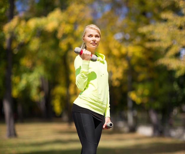 Concetto di sport e stile di vita - giovane donna sportiva con manubri leggeri all'aperto