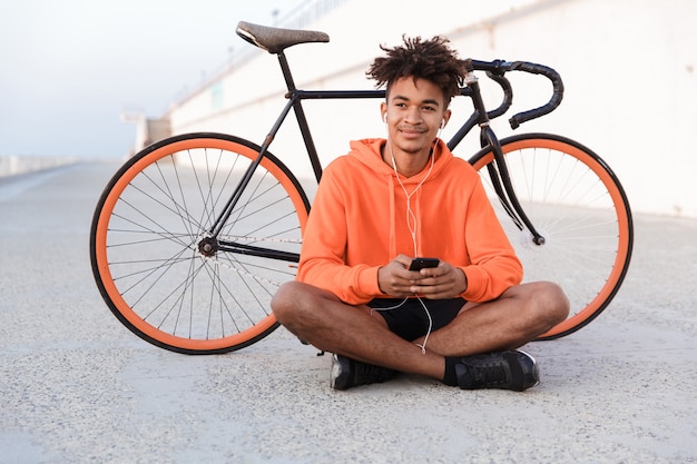 Sport man buiten op het strand met fiets met behulp van mobiele telefoon luisteren muziek