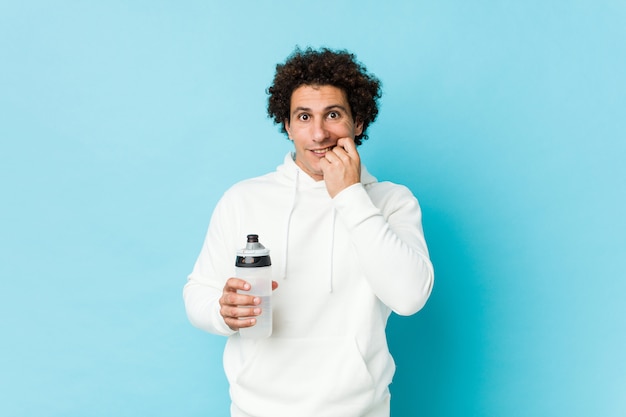 Sport man holding a water bottle biting fingernails, nervous and very anxious.