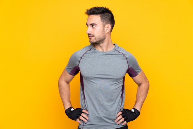 Sport man over isolated yellow wall posing with arms at hip and looking side