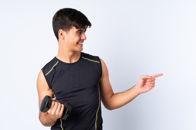 Sport man making weightlifting over isolated blue background pointing to the side to present a product