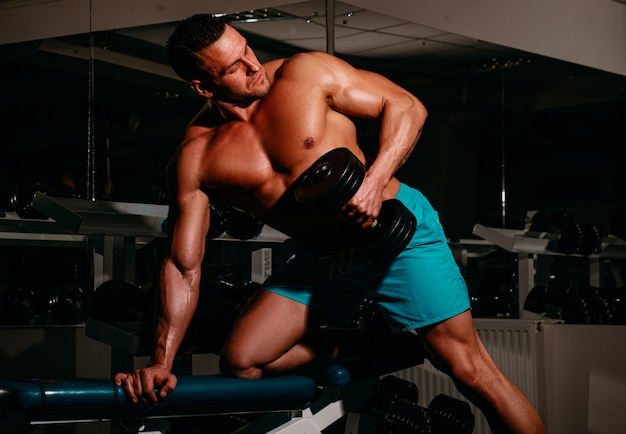 Спортивный мужчина делает упражнения на бицепс в тренажерном зале портрет молодого спортсмена, выполняющего упражнения с гантелями