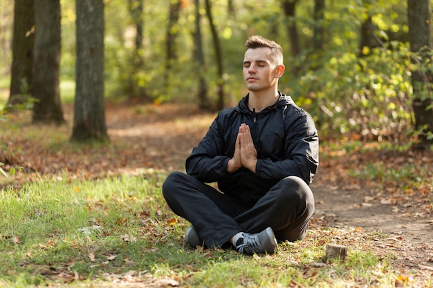 Sport man meditates in the lotus position in the autumn forest