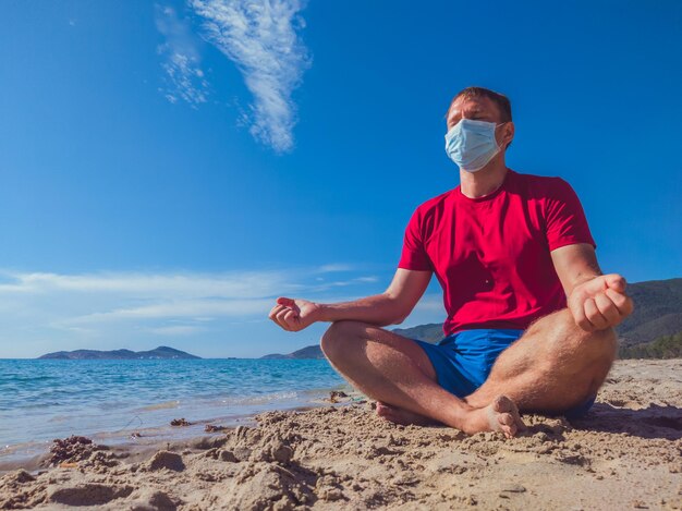 Sport man met medisch masker doet buiten trainingen in het park in de buurt van zee tijdens pandemische quarantaine Geestelijke bescherming ademhaling energie oefening uitademing inademing concentratie meditatie yoga pose