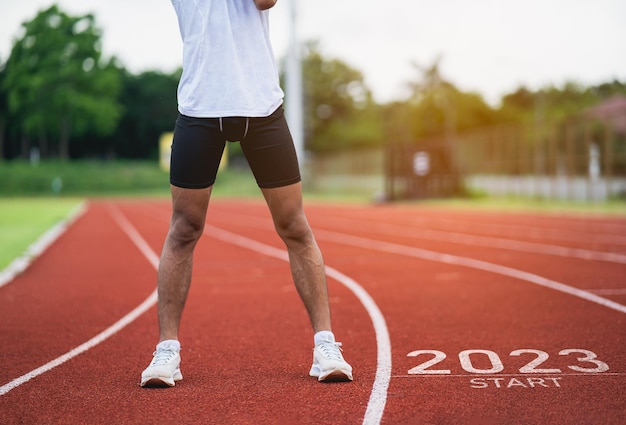 Sport man runner stretching at running track start into the new year 2023 Start up of runner man running at stadium go to Goal of Success People running as part of Number 2023 Sport health care