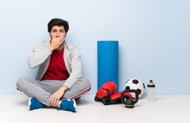 Sport man sitting on the floor covering mouth with hands