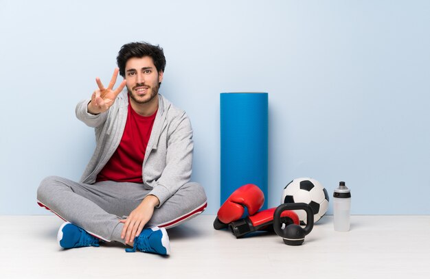 Sport man sitting on the floor happy and counting three with fingers