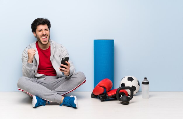 Sport man sitting on the floor with phone in victory position