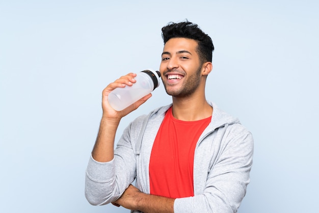 Sport man with a bottle of water over isolated blue wall