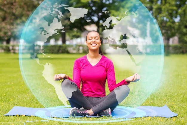 Foto concetto di sport, meditazione, parco e stile di vita - donna sorridente che medita sul tappetino all'aperto
