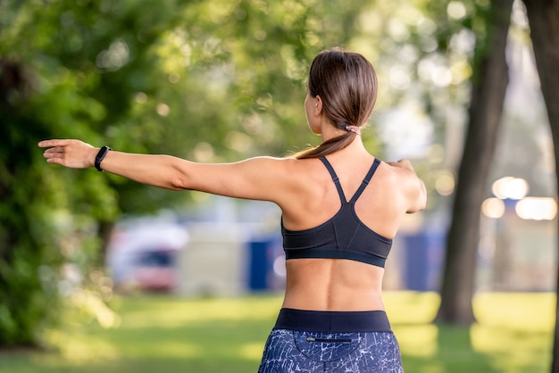 Sport meisje doet yoga training in de natuur in de ochtend. Jonge vrouw oefenen en strekken armen buitenshuis portret van achteren