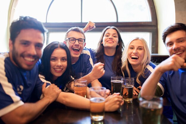 sport, mensen, vrije tijd, vriendschap en entertainment concept - gelukkige voetbalfans of vrienden die bier drinken en de overwinning vieren in de bar of pub