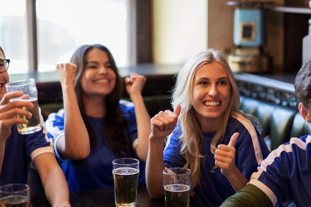 sport, mensen, vrije tijd, vriendschap en entertainment concept - gelukkige voetbalfans of vrienden met bier kijken naar spel en overwinning vieren in bar of pub