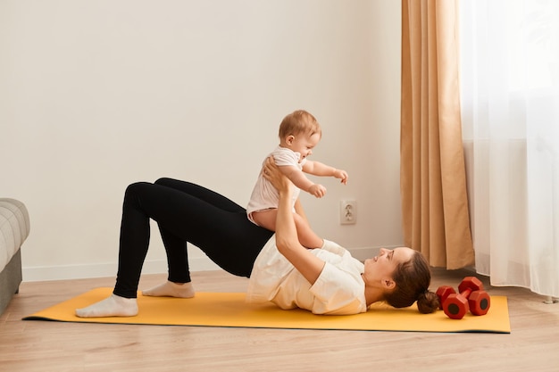 Sport moederschap en actieve levensstijl zijaanzicht van jonge moeder training samen met haar baby die plezier heeft en speelt met haar dochtertje terwijl ze oefeningen voor peuken doet