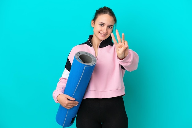 Sport Oekraïense vrouw die naar yogalessen gaat terwijl ze een mat blij houdt en drie telt met vingers