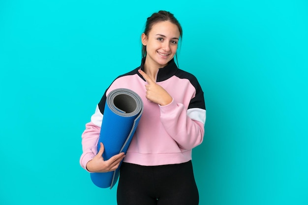 Sport Oekraïense vrouw die naar yogalessen gaat terwijl ze een mat vasthoudt die naar de zijkant wijst om een product te presenteren