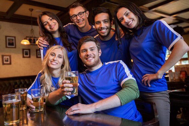 sport, people, leisure, friendship and entertainment concept - happy football fans or friends drinking beer at bar or pub