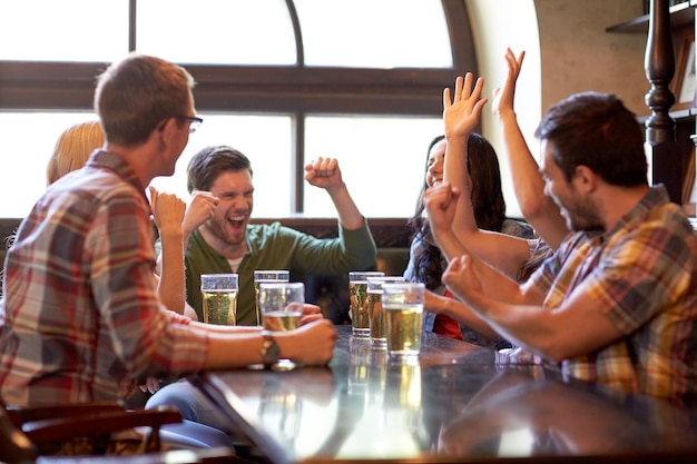 концепция спорта, людей, отдыха, дружбы и развлечений - счастливые футбольные фанаты или друзья пьют пиво и празднуют победу в баре или пабе