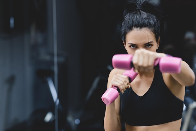 Sport people and liefstyle concept Horizontal closeup portrait of strong young woman doing exercise with dumbbells Fitness female doing intense training in the gym