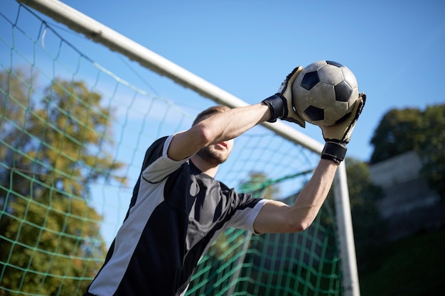 sport and people - soccer player or goalkeeper catching ball at football goal on field