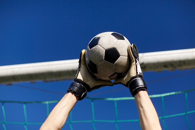 Foto sport e persone - le mani del calciatore o del portiere che prendono la palla alla porta di calcio sopra il cielo blu