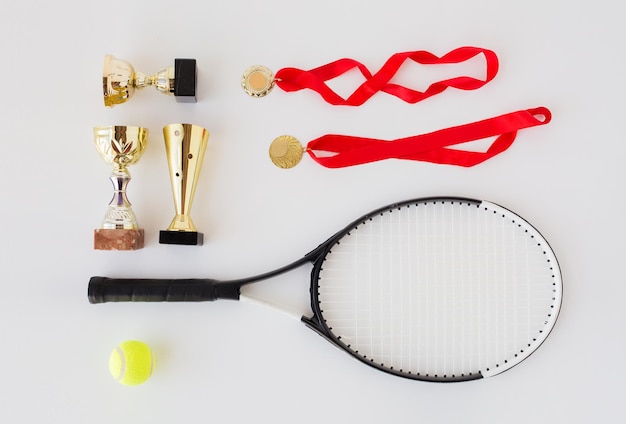 sport, prestatie, kampioenschap, competitie en succes concept - close-up van tennisracket en bal met bekers en medailles op witte achtergrond